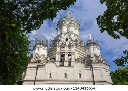 Christian white temple with bells against the blue sky with clouds and green foliage