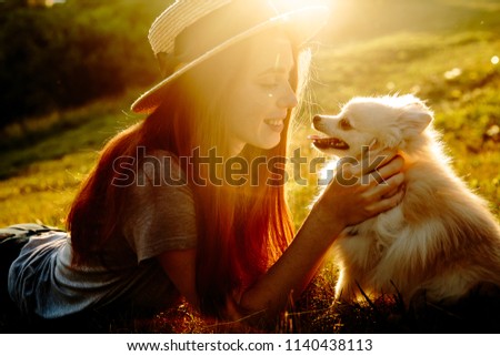 The cute red-haired woman in a hat with a spitz-dog lying in the park. Beautiful sunset light. Background toning for instagram filter.