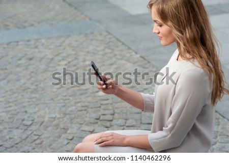 Young elegant blonde female with smartphone outdoors