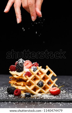 Photo of viennese wafers with raspberries, strawberries sprinkled with powdered sugar on blackboard against blank background