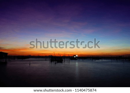 
Long exposure shot Sunset over lake with silhouette fishinng home,boat and indutstrail fishing on foreground at southern Thailand background.
