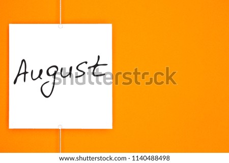 Paper card (photo frame) with handwritten text August  hanging on metal rope with magnets on orange background