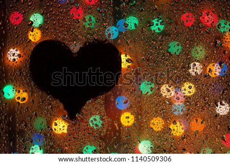 Bright festive background and colored bokeh. Silhouette of a heart against a background of drops of water on a glass