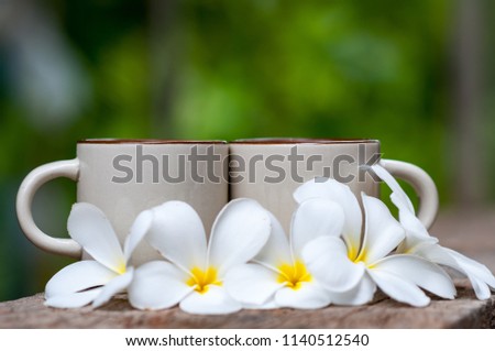 Coffee cup is placed on an old wooden floor and has plumeria flower placed next to it. Background is green and soft. Concept of this picture is refreshing with morning coffee and beautiful flower.