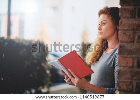 Woman reading book outdoors while leaning on the wall.