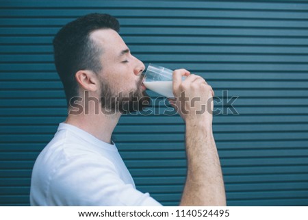 A picture of man drinking milk from glass. He is keeping eyes closed. Isolated on striped and blue background.