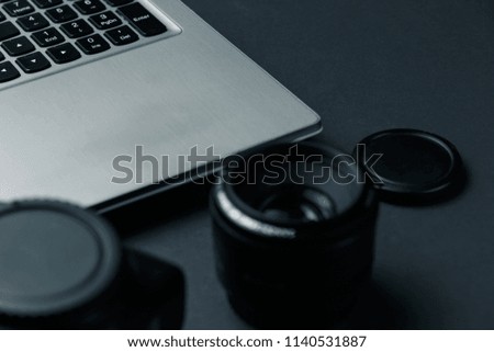 Work space on black table of photographer. Minimal workspace with Laptop, camera and lens copy space on dark background. Modern and elegant. Close up.