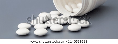 White round pills scattered from a white jar on a gray background.