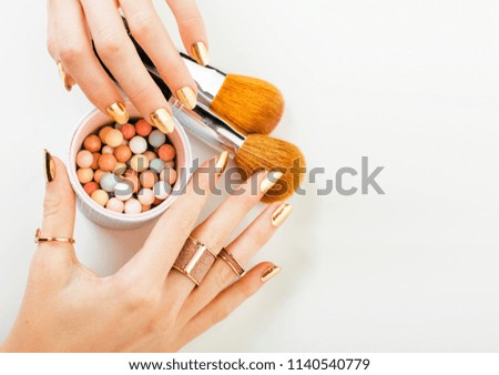woman hands with golden manicure and many rings holding brushes,