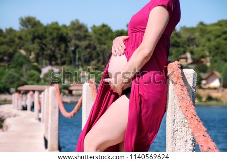 Beautiful pregnant woman and lady is hugging and holding her pregnant belly, standing in natural environment. Waiting for baby. Mom holds hands on belly on sea and sky nature background. Pregnancy.