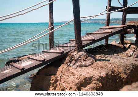 Colorful picture with an old bridge that lies on the rough rock. Bright colors of the picture. Nice blue sea beyond the bridge. Closeup. Sunny summer day. Beautiful background. 