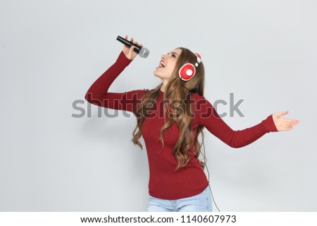 Young woman singing into microphone on color background. Christmas music