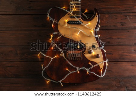 Guitar with fairy lights on wooden background. Christmas music concept