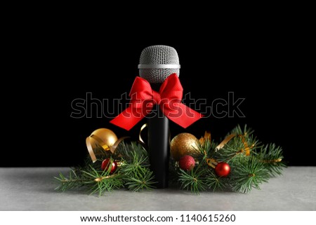 Microphone with bow and decorations on table against black background. Christmas music concept