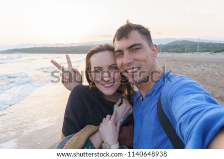 Selfie smiling couple in love on the beach at sunset with a symbol of peace. Concept of travel, love, recreation, adventure, family