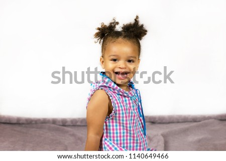 Waist-up portrait of lovely african baby girl smiling happily and looking at camera. Cute little american child wearing amazing colourful dress. Childish concept