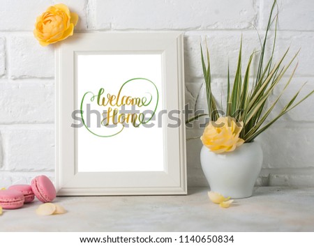 Mockup of picture frame decorated with macaroons and yellow roses on white brick background.  Welcome home words.