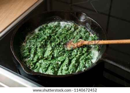 Preparation of a dish - baby spinach boiled in garlic sauce in a cast-iron pan.  Royalty-Free Stock Photo #1140672452