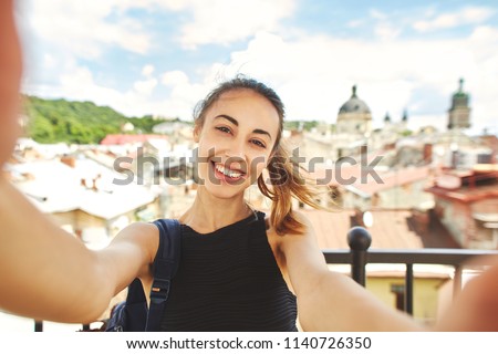 selfie portrait of attractive woman tourist walking in the center of old city of Lviv. woman admires the view of the cityscape from the rooftop with wonderful cloudy blue sky on background and making