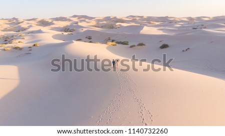 Romantic latin couple walking in the white dunes desert leaving footprints behind them. Samalayuca, Chihuahua, Mexico. Aerial shot.