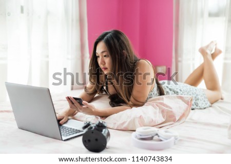 Attractive Asian beautiful woman on bed shop on website and pay by typing credit card name, 16 digit number, and security code to laptop computer. Girl hold magnetic card to shopping online.