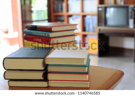 A close-up view of a stack of colorful books on a table in a library with light from a window bookshelf is the background selective focus and shallow depth of field