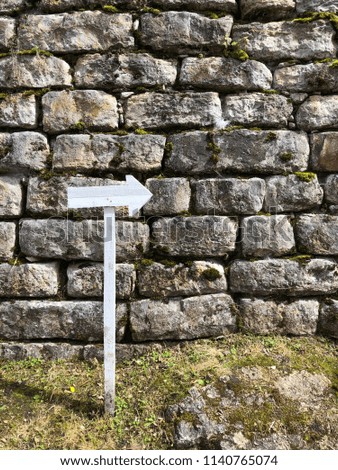 White wooden arrow sign pointing to the right in front of an ancient wall at the Kuelap archaeological site in Chachapoyas, Amazonas, Peru