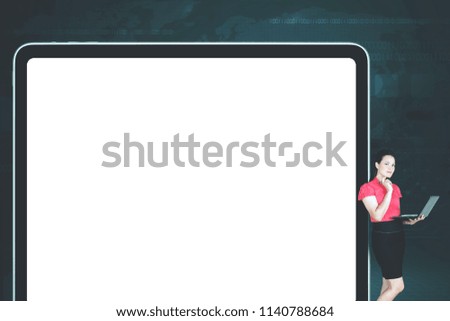 Picture of Caucasian businesswoman working with a laptop while thinking idea and leaning on a blank screen of big tablet