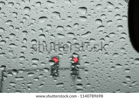 Rain drops on the car glass while the car is red. On the city street

