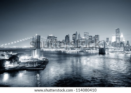New York City Manhattan downtown skyline aerial view black and white at dusk with skyscrapers lit over East River with reflections.