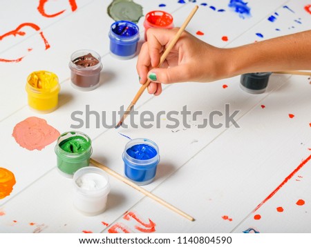 Hand girl with colorful nails paint a white table.
