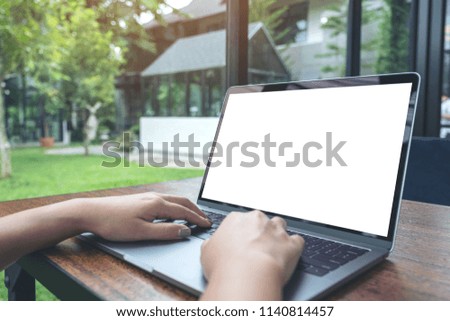 Mockup image of a woman using and typing on laptop with blank white desktop screen on wooden table and green nature background 