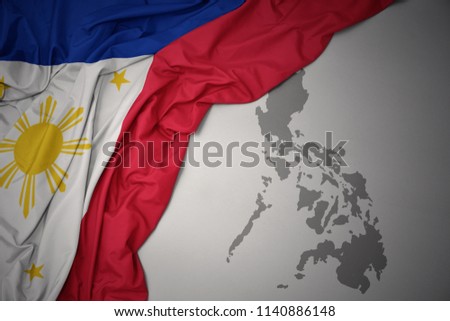 waving colorful national flag of philippines on a gray map background.