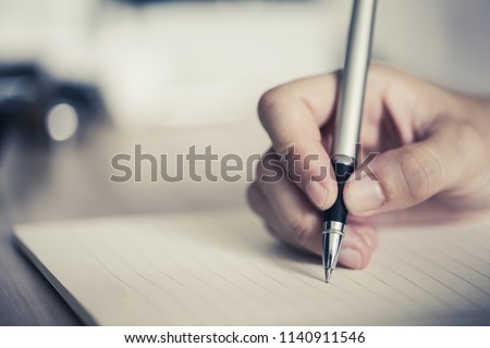 Close shot of a human hand writing something on the paper. Royalty-Free Stock Photo #1140911546