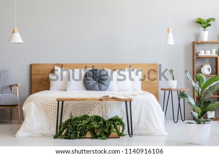 Blue pillow on white bed with wooden headboard in bedroom interior with plants. Real photo