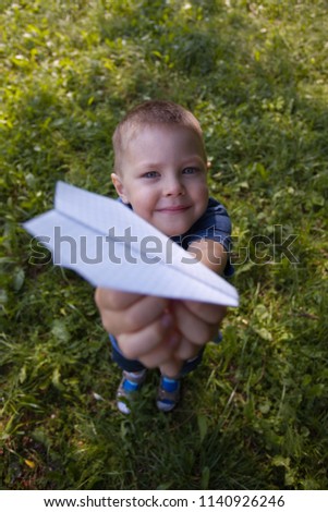 Paper airplane in kid hands close-up. Toddler boy 4 years old holding origami plane in park or garden in shadoow in summer sunny day. Hobby, leisure, entertainment, handmade, craft concept