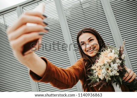 Positibve girl takes selfie. She smiles on camera. Woman holds flowers. She looks happy. Isolated on striped and white background