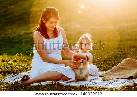 Mother and daughter in park with dog smiling. Sunset. Horizontal photo