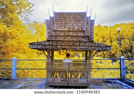 The young man sitting in the pavilion beside the fence with yellow trees from near infrared style by IR mode.Paradise concept.        