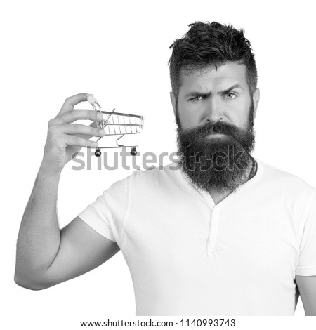 e-commerce and shopping concept. Bearded man wearing white t-shirt holding mini shopping cart on right hand. Closeup portrait of businessman showing mini shopping cart, online shop, ecommerce concept