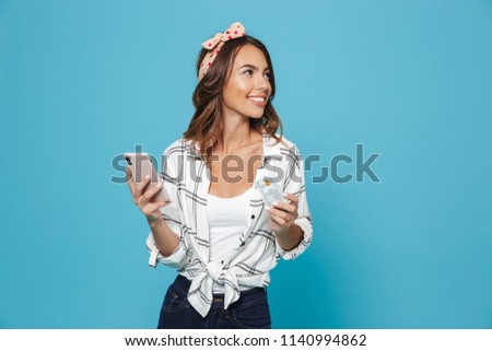 Portrait of european cute woman 20s wearing headband smiling while holding mobile phone and credit card isolated over blue background