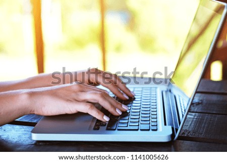 Woman's hands typing on laptop outdoors. Sunny nature background