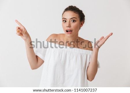 Portrait of a cheerful young casual brunette woman pointing at copy space isolated over white background