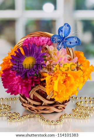 Beautiful bouquet of bright flowers in small basket with paper note on white table on window background