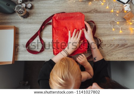 Woman's hands wrapping handmade present in paper with red ribbon.