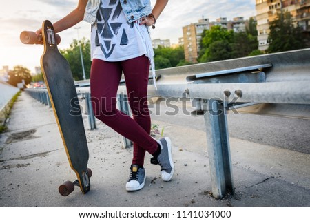 Young urban skate gitl holding long-board in the street - detail. Urban youth culture