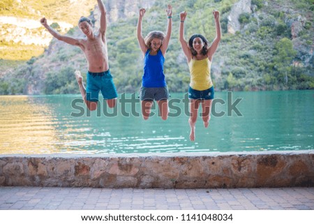 Friends jumping on a embankment on a turquoise lake in the mountains 