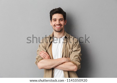 Portrait of a happy young casual man standing with arms folded isolated over gray background