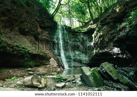 Beautiful mountain rainforest waterfall with fast flowing water and rocks, long exposure. Natural seasonal travel outdoor background in hipster vintage style