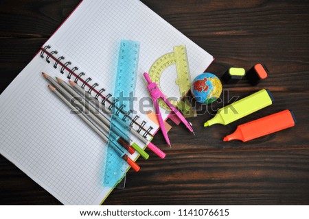 stationery scattered on a notebook lying on a dark wooden table, top view